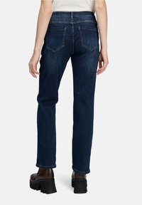 Person wearing dark blue straight-leg jeans and brown chunky-heeled ankle boots, standing against a plain background.