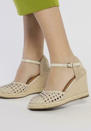 Sandalias de cuña tejidas en beige con diseño de punta descubierta, correa al tobillo y tacón texturizado. La suela está hecha de material de yute.