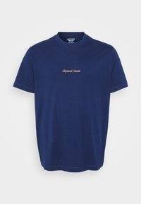 Camiseta de algodón azul marino con cuello redondo y mangas cortas; "Originals Studio" bordado en hilo color marrón en el pecho.