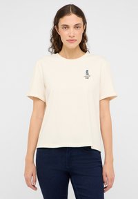 Kremowa, krótki rękaw t-shirt uszyty z miękkiej bawełny, z małym graficznym wzorem na lewej części klatki piersiowej.