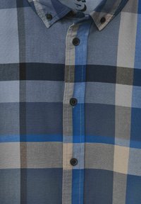 Camicia a quadri blu e grigia con colletto rigido, bottoni neri e motivi a quadri di diverse tonalità chiare e scure.