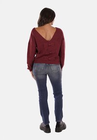 Maglione a maglia bordeaux con uno scollo a V profondo, decorato con tre fiocchi. Abbinato a jeans fitted blu scuro e scarpe con piattaforma nere.
