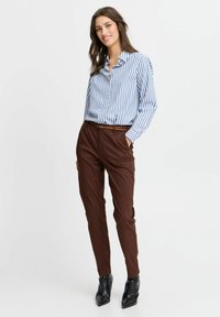 Gestreiftes blaues und weißes Langarmhemd mit Knöpfen, kombiniert mit braunen maßgeschneiderten Hosen; schwarze High Heels Stiefeletten. Glatter Stoff und figurbetonter Schnitt.