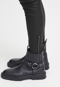 Svarta läderankelboots med ribbade detaljer, silverfärgad hårdvara och en kraftig sula; kombinerat med figurnära svarta byxor med blixtlås.