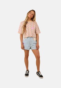 Pull à manches courtes multicolore avec un motif en losange, associé à un short en denim bleu clair. Baskets noir et blanc avec lacets.