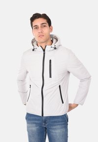 Giacca leggera bianca con cappuccio realizzata in materiale liscio. Presenta zip nere, due tasche laterali e una tasca sul petto con zip.
