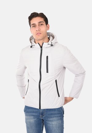 Giacca leggera bianca con cappuccio realizzata in materiale liscio. Presenta zip nere, due tasche laterali e una tasca sul petto con zip.