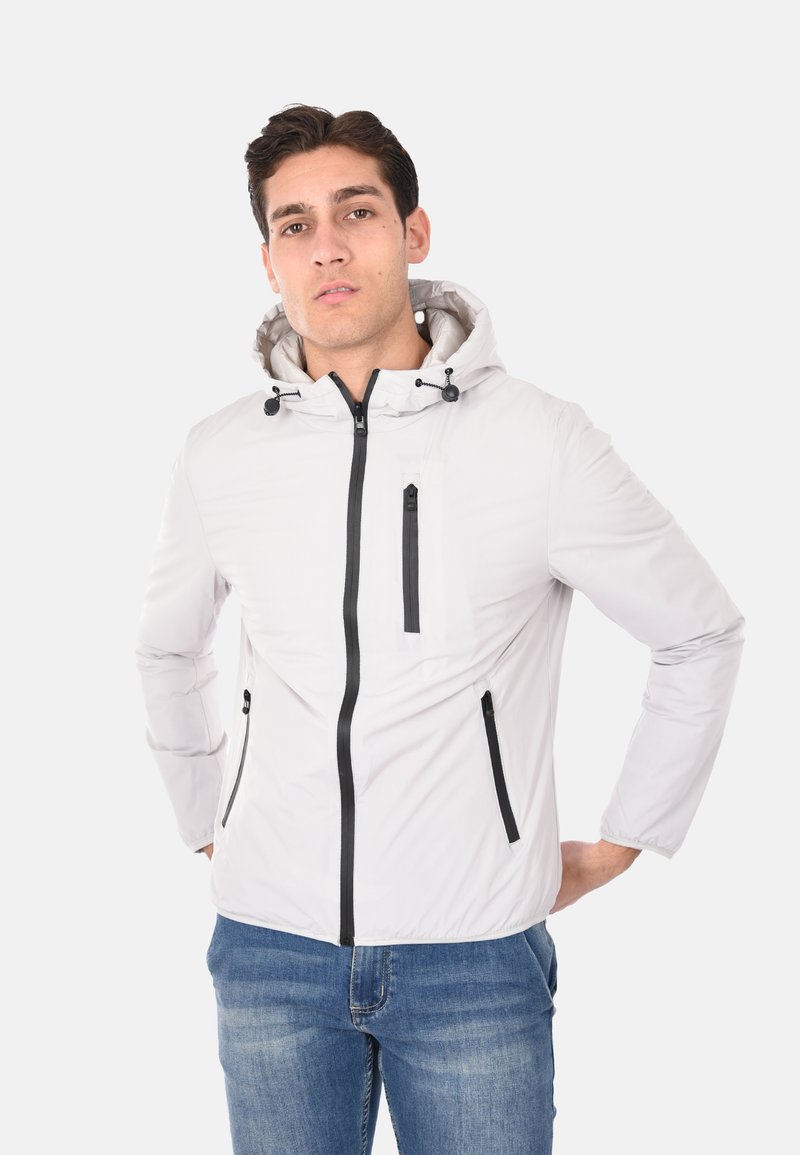 Giacca leggera bianca con cappuccio realizzata in materiale liscio. Presenta zip nere, due tasche laterali e una tasca sul petto con zip.