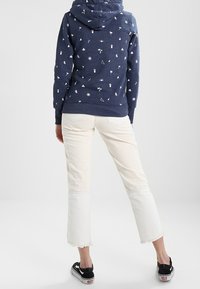 Felpa navy con motivi geometrici e naturali bianchi, abbinata a jeans cropped crema con orli a taglio vivo e sneakers nere.