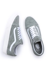 Šedé semišové tenisky Vans s bílými tkaničkami a podrážkami, s viditelným bočním pruhem a logem uvnitř pravé boty, na bílém pozadí.