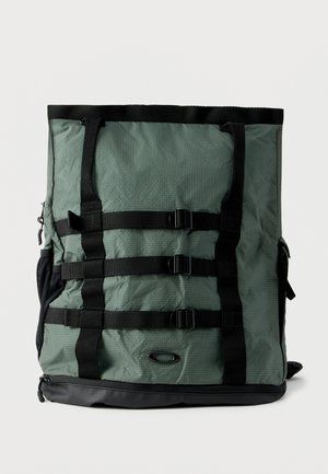 Kõrge roheline seljakott mustade rihmade, kolme horisontaalse pandla, küljetaskute ja musta põhjakihiga.