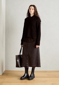 Suéter de punto negro superpuesto a una camiseta negra, combinado con una larga falda de mezclilla negra y botines negros. Incluye un bolso tote oscuro.