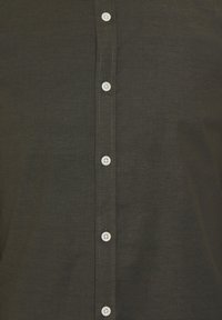 Donkergroen overhemd met knopen, gemaakt van stof met een gladde textuur; heeft witte knopen in het midden en zichtbare stiksels.