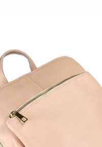 Lichtroze leren rugzak met een gouden rits op het voorvak en een kort handvat aan de bovenkant.