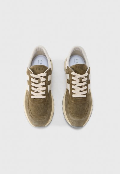 Πράσινα σουέτ αθλητικά παπούτσια με τρεις λευκές ρίγες, στρογγυλή μύτη και μπεζ λαστιχένια σόλα. Διαθέτουν εκρού κορδόνια και επενδυμένο γιακά.