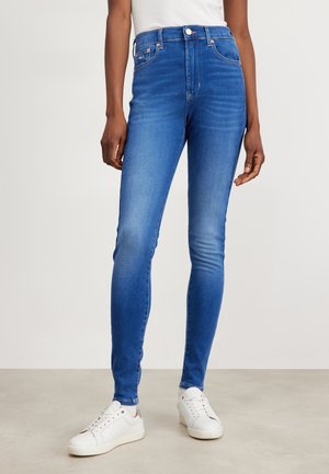 Jeans ajustados de talle alto en mezclilla azul medio con una textura suave. Presentan pasadores para cinturón, un botón en la parte delantera y un desvanecimiento mínimo.