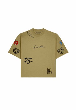 Vrouw draagt een beige oversized T-shirt met zwarte grafische tekst en tekeningen, een zwarte zonnebril en haar in een knotje.