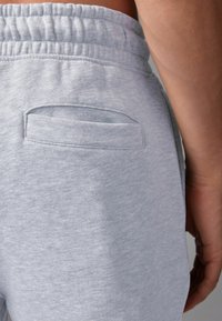 Pantalones de chándal grises con una cinturilla elástica, que cuentan con un bolsillo trasero plano. La tela tiene un acabado suave y texturizado.