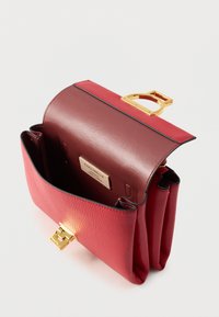 Borsa a mano in pelle rossa con finitura testurizzata, dotata di fibbia in metallo dorato e etichetta interna con il marchio. Design aperto con tre scomparti.
