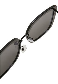 Mustad mustat cat-eye päikeseprillid tumedate objektiividega, metallaktsentidega ja läbipaistvate silikoonist nina padjanditega. Nurgeline, stiilne disain kergest raamist.