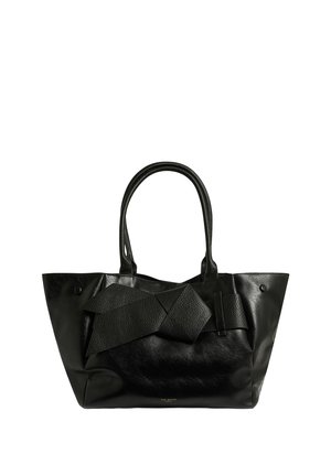 Sac cabas en cuir noir avec un grand nœud texturé sur le devant et deux poignées doubles.