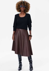 Ciemny sweter z prążkowanej dzianiny i okrągłym dekoltem, połączony z brązową skórzaną spódnicą w kształcie litery A. Czarne kozaki do kolan dopełniają całość.