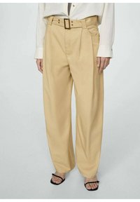 Beige wijde broek met een hoge taille, voorzien van een riem met een rechthoekige gesp en geplooide details. Glad stofgevoel.