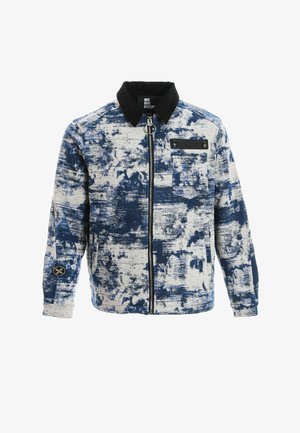 Chaqueta de hombre con patrón abstracto en azul y blanco, cuello negro, cremallera frontal, bolsillo en el pecho y detalle de parche en la manga izquierda.