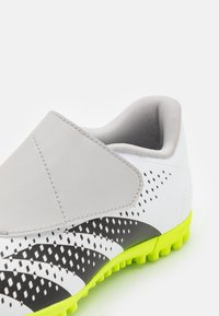 Gray slip-on soccer shoes with a textured upper, black and white design accents, and bright yellow rubber cleats. Smooth surfaces and pattern details.