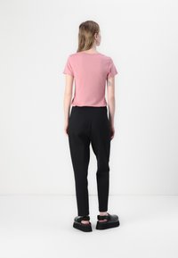 Roze T-shirt met korte mouwen, gecombineerd met zwarte taps toelopende broek en stevige zwarte sandalen. Glad materiaal en een eenvoudig ontwerp zonder patronen.