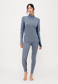 Mönstrad blå och vit långärmad topp och leggings med en figurnära design, som har en hög krage och kontrasterande marinblå sidopaneler.