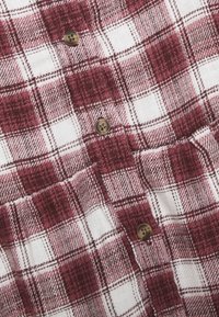 Gros plan sur un tissu à carreaux rouge et blanc avec des boutons marron cousus sur le devant d'une chemise.