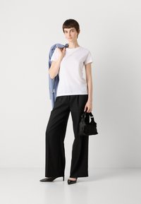 White cotton t-shirt, black wide-leg trousers, black pointed heels, holding a black textured handbag, with a light blue blazer draped on shoulder.