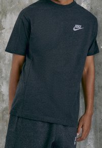 Dark gray cotton T-shirt with short sleeves, featuring a white Nike logo on the left chest. Smooth texture and relaxed fit.
