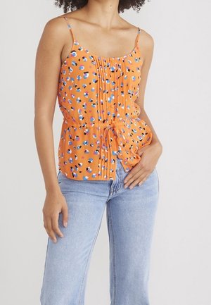 Orange Blumentop mit verstellbaren Spaghetti-Trägern, einem gerafften Vorderteil und einer Schleifen-Detailung an der Taille, kombiniert mit hellblauen Jeans.