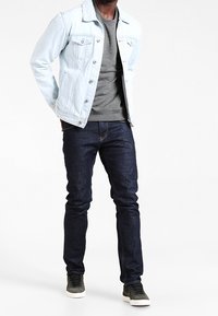 Giacca di jeans blu chiaro, t-shirt grigia, jeans blu scuro e sneakers grigie. Design semplice con bottoni e tasche sulla giacca.