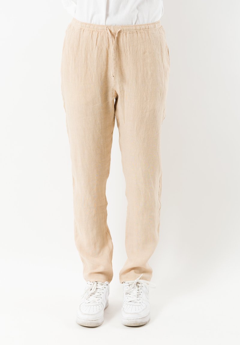 Licht beige linnen broeken met een elastische tailleband, zijzakken en een relaxte pasvorm, gestyled met witte sneakers.