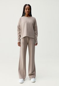 Felpa oversize beige con spalle cadute abbinata a pantaloni larghi coordinati. Texture liscia e design minimalista.