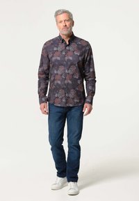 Lange mouw knoopshirt met een donker bloemenpatroon in paarse en witte tinten, gecombineerd met blauwe jeans en witte sneakers.