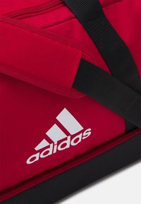 Rode stoffen reistas met zwarte accenten. Voorzien van een rits en een opvallend wit Adidas-logo. Duurzaam ontwerp met stevige schouderbanden.