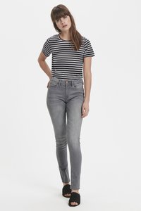 Camiseta de manga corta a rayas con escote redondo, combinada con jeans ajustados grises. El modelo lleva sandalias negras de dedos al aire.