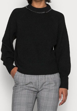 Zwarte ribgebreide trui met een ronde halslijn, voorzien van een metallic kettingaccent langs de kraag en mouwen met een losse pasvorm. Gedoeld in combinatie met een geruit broek.