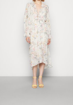 Robe à manches longues à fleurs avec un col et des poignets à volants, présentant des couleurs pastel et un ourlet à niveaux ; assortie à des sandales jaunes à lanières.