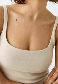 Beige ribbad linne med fyrkantig halsringning och breda axelremmar, med en smidig textur och figurnära design som framhäver nyckelbenet.