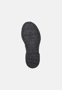 Black rubber shoe sole with textured tread pattern, featuring a circular design at the heel and branding in the center.