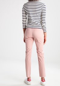 Pantaloni rosa chiaro con una vestibilità slim, abbinati a una maglietta a maniche lunghe a righe blu e bianche. Dettagli delle cuciture e vita visibili. Sneakers bianche.