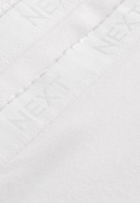 Biely odev s hladkou, mäkkou textúrou. Obsahuje šitú etiketu s vyrazeným nápisom "NEXT" pozdĺž horného okraja.
