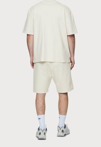 Ljusbeige bomulls t-shirt och shorts-set, med en avslappnad passform. Enkel design utan synliga mönster. Bärs med vita strumpor och sneakers.