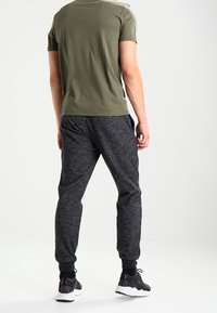 Olive green short-sleeve shirt with muted texture, paired with dark gray jogger pants featuring elastic cuffs and a heathered finish. Black sneakers.