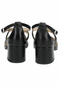Talons noirs en cuir avec un talon épais, une sangle à la cheville et des découpes latérales. Texture lisse avec un design élégant et un petit accent en boucle en argent.